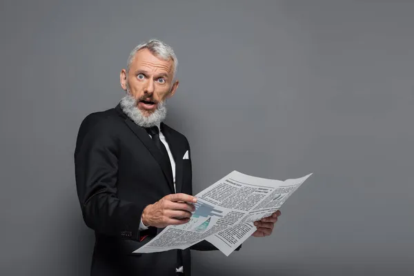 Surprised middle aged businessman holding newspaper on grey — Stock Photo