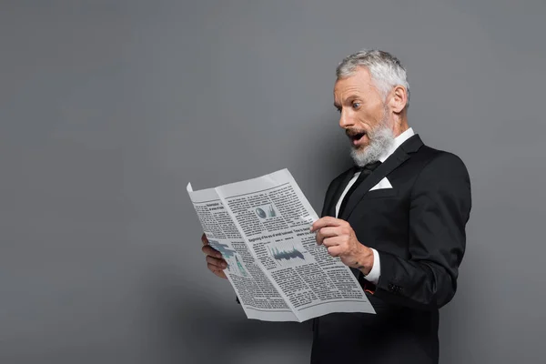 Shocked middle aged man in suit reading newspaper on grey — Stock Photo