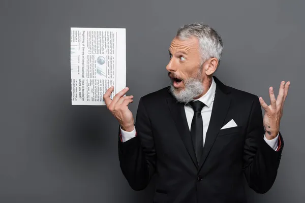 Verblüffter Geschäftsmann mittleren Alters gestikuliert, während er Zeitung auf grau hält — Stockfoto