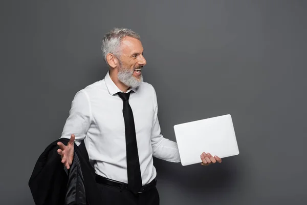 Hombre de mediana edad feliz sosteniendo portátil y chaqueta en gris - foto de stock