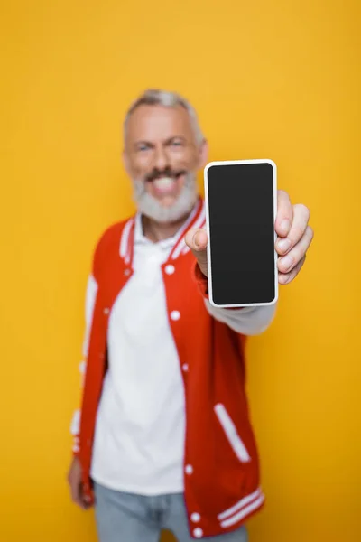 Felice e sfocato uomo di mezza età che tiene smartphone con schermo bianco isolato su giallo — Foto stock