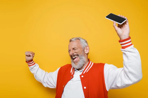 Щасливий чоловік середнього віку з закритими очима тримає смартфон з порожнім екраном на жовтому — стокове фото