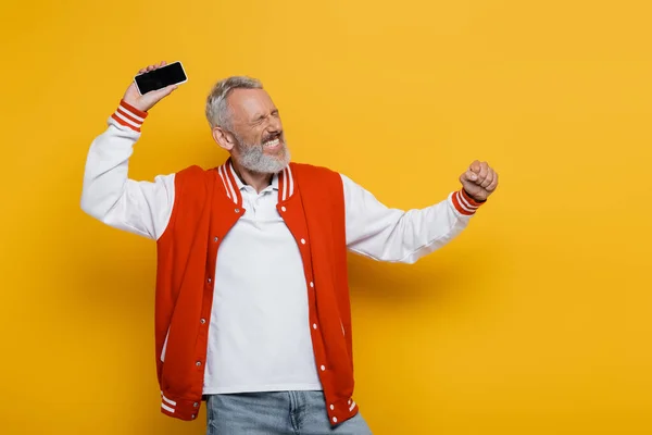 Happy middle aged man with closed eyes holding cellphone with blank screen on yellow — Stock Photo
