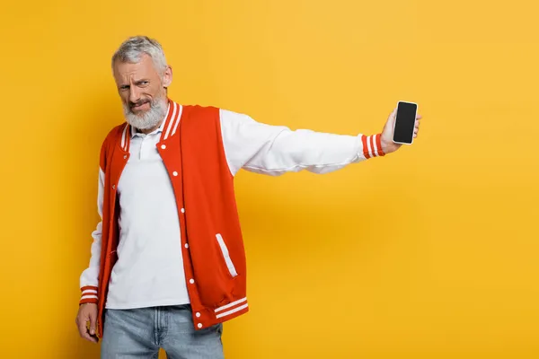 Homem de meia idade descontente segurando smartphone com tela em branco isolado no amarelo — Fotografia de Stock