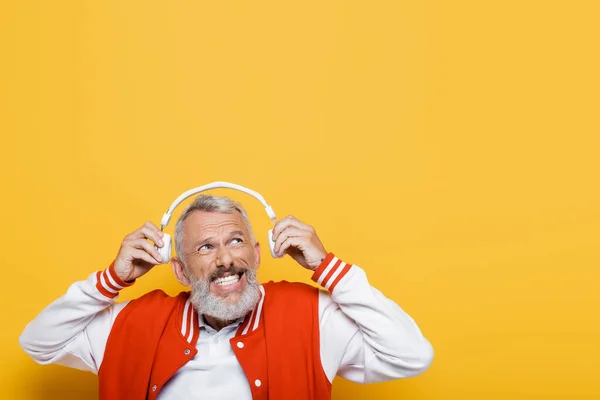 Hombre de mediana edad positivo sosteniendo auriculares inalámbricos aislados en amarillo - foto de stock