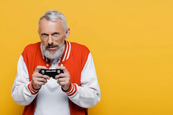 KYIV, UKRAINE - JULY 29, 2021: tensed middle aged man in bomber jacket holding joystick and playing video game isolated on yellow — Stock Photo