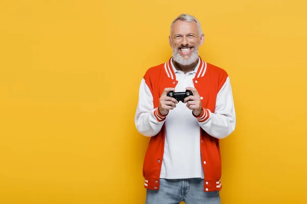 KYIV, UCRANIA - 29 de julio de 2021: feliz hombre de mediana edad con chaqueta de bombardero con joystick aislado en amarillo - foto de stock