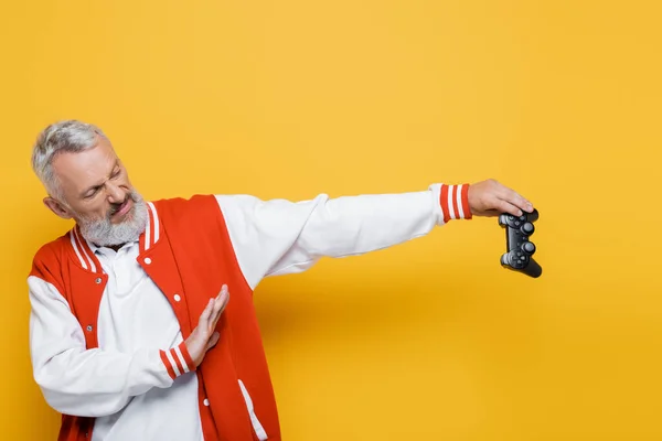 KYIV, UKRAINE - JULY 29, 2021: displeased man in bomber jacket holding joystick and showing no gesture on yellow — Stock Photo