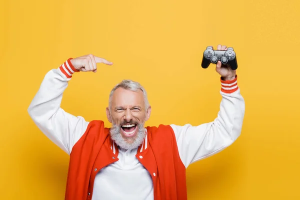 KYIV, UKRAINE - JULY 29, 2021: happy middle aged man in bomber jacket pointing at joystick on yellow — Stock Photo