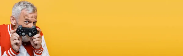 KYIV, UKRAINE - JULY 29, 2021: middle aged man in bomber jacket covering face with joystick isolated on yellow, banner — Stock Photo