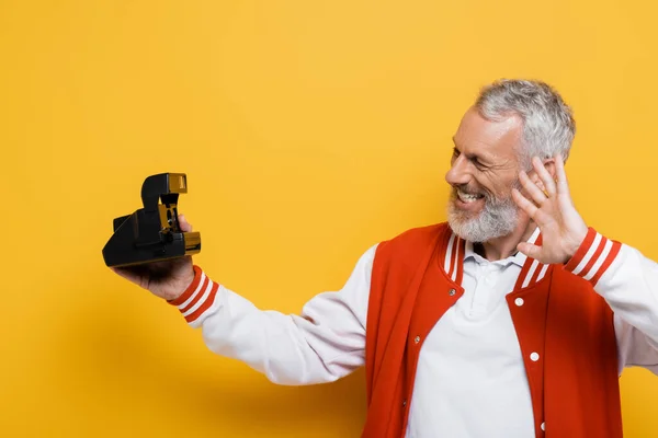 Heureux homme d'âge moyen en veste de bombardier prendre selfie sur caméra vintage noire sur jaune — Photo de stock