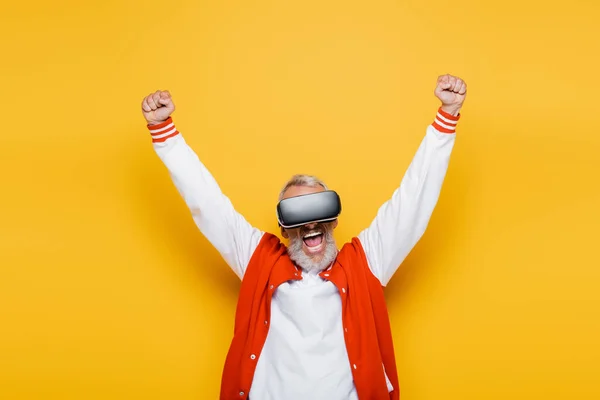 Excited middle aged man in bomber jacket and vr headset rejoicing on yellow — Stock Photo