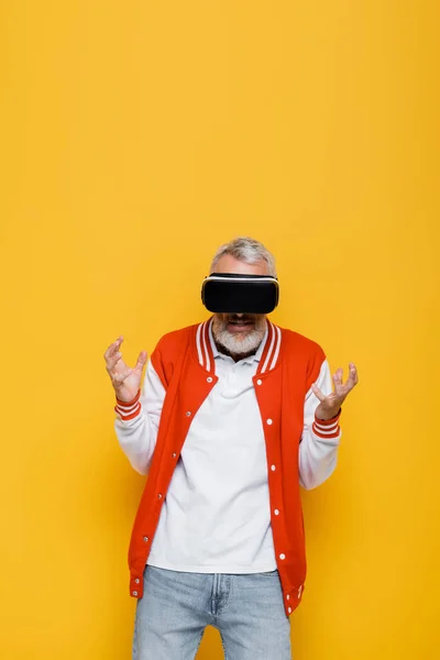 Hombre de mediana edad en chaqueta de bombardero y auriculares vr gesto aislado en amarillo - foto de stock