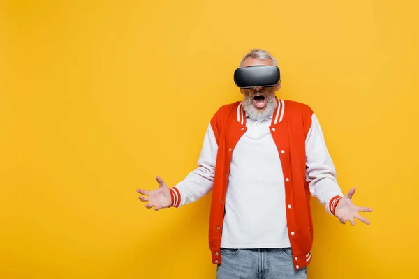 Sorprendido hombre de mediana edad en chaqueta de bombardero y auriculares vr en amarillo - foto de stock