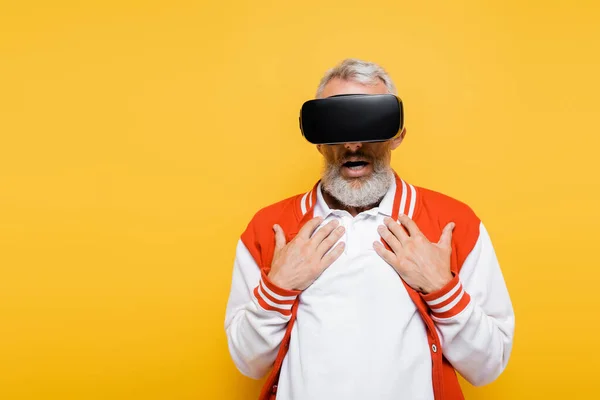 Sorprendido hombre de mediana edad en chaqueta de bombardero y auriculares vr aislados en amarillo - foto de stock