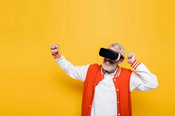 Smiling middle aged man in bomber jacket and vr headset gesturing on yellow — Stock Photo