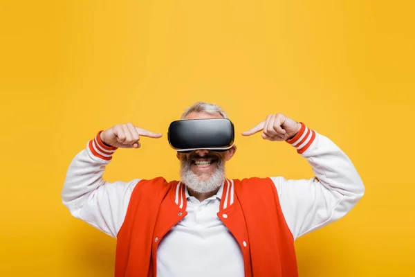 Happy middle aged man in bomber jacket pointing at vr headset on yellow — Stock Photo