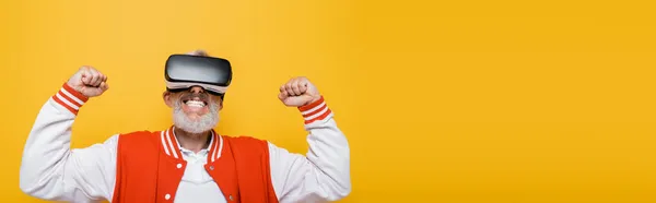 Hombre de mediana edad en chaqueta de bombardero y auriculares vr regocijo aislado en amarillo, bandera - foto de stock