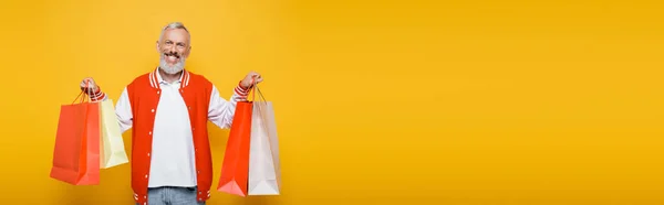 Glücklicher Mann mittleren Alters in Bomberjacke mit Einkaufstüten auf gelbem Banner — Stockfoto