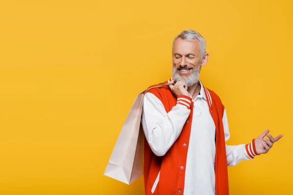 Happy middle aged man in bomber jacket holding shopping bag isolated on yellow — Stock Photo