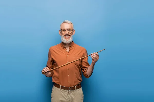 Cheerful middle aged teacher in glasses holding pointer stick on blue — Stock Photo