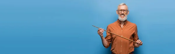 Happy middle aged teacher in glasses holding pointer stick on blue, banner — Stock Photo