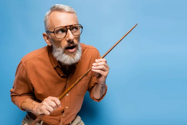 Profesor de mediana edad en gafas sosteniendo puntero palo y mirando hacia otro lado en azul - foto de stock