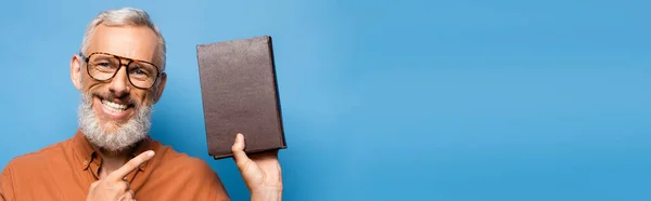 Feliz professor de meia-idade em óculos apontando para o livro em azul, banner — Fotografia de Stock