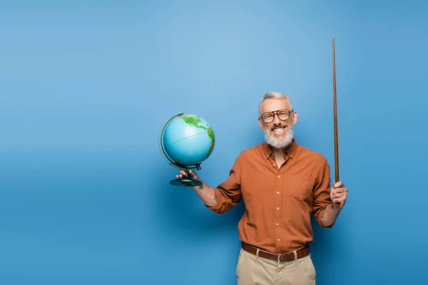 Cheerful middle aged teacher in glasses holding pointer stick and globe on blue — Stock Photo