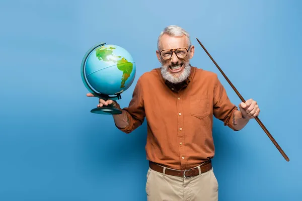 Excited middle aged teacher in glasses holding pointer stick and globe on blue — Stock Photo