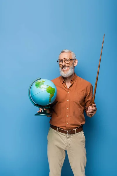 Щасливий вчитель середнього віку в окулярах тримає вказівник палицю і глобус на синьому — стокове фото