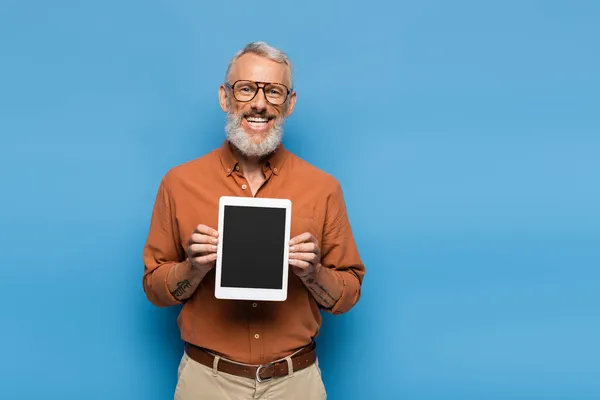 Happy middle aged man in glasses and shirt holding digital tablet with blank screen on blue — Stock Photo