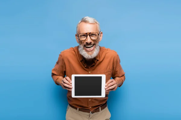 Alegre hombre de mediana edad en gafas y camisa sosteniendo tableta digital con pantalla en blanco en azul - foto de stock