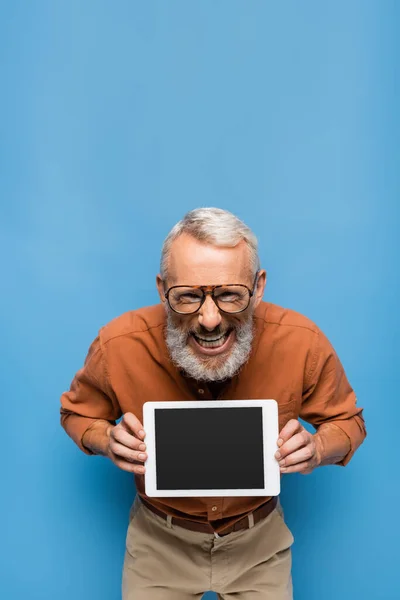 Homme d'âge moyen souriant dans des lunettes et chemise tenant tablette numérique avec écran blanc sur bleu — Photo de stock