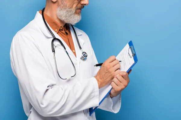 Vista recortada del médico de mediana edad en blanco abrigo escribir prescripción en portapapeles en azul - foto de stock