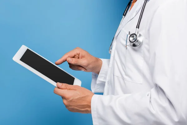 Обрізаний вид лікаря середнього віку в білому пальто, що вказує на цифровий планшет з порожнім екраном на синьому — стокове фото