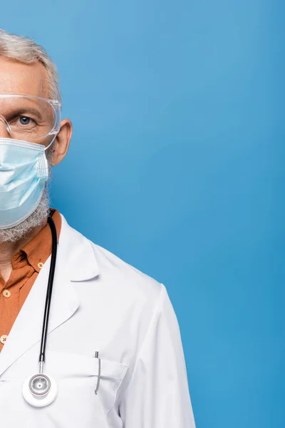 Cropped view of middle aged doctor in white coat, medical mask and goggles on blue — Stock Photo