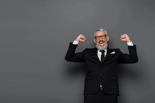 Excité homme d'âge moyen en costume et lunettes se réjouissant sur gris — Photo de stock