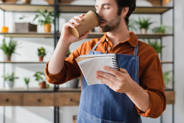 Notebook in hand of blurred seller drinking coffee in flower shop — Stock Photo