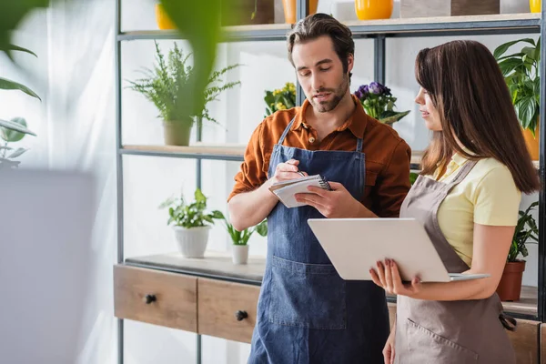 Floristas con portátil y portátil hablando cerca de las plantas en la tienda - foto de stock