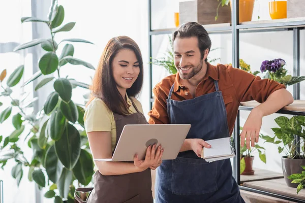 Fioristi positivi con computer portatile e notebook che lavorano vicino a impianti in negozio — Foto stock