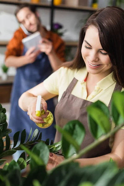 Fiorista sorridente che spruzza impianti in negozio di fiori — Foto stock