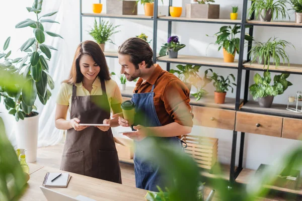 Giovani fioristi con caffè utilizzando garget in negozio di fiori — Foto stock