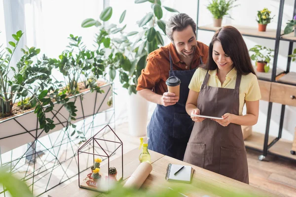 Fröhliche Floristen mit Pappbecher mit digitalem Tablet im Blumenladen — Stockfoto