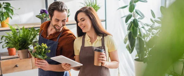 Floristin zeigt Kollegen mit Pflanzen im Geschäft digitales Tablet, Banner — Stockfoto