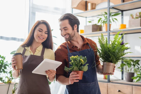 Jóvenes vendedores sosteniendo plantas y tableta digital en floristería - foto de stock