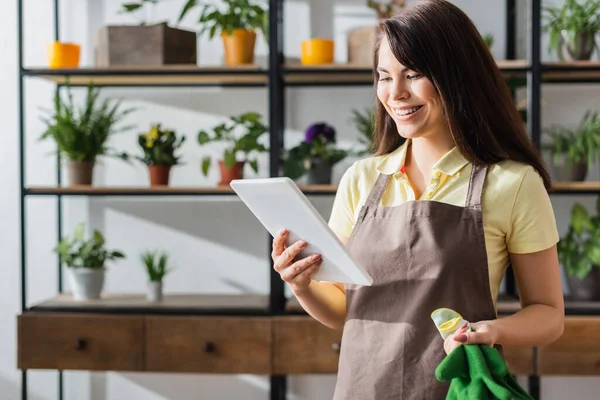 Cheerful florist holding gloves and digital tablet in flower shop — Stock Photo