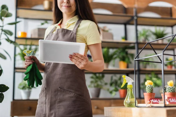 Cropped view of seller holding digital tablet and gloves in flower shop — Stock Photo