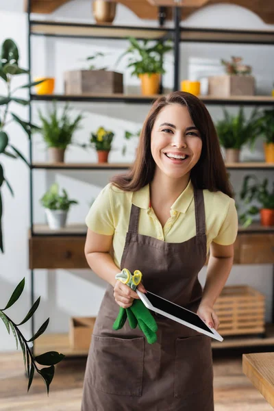 Positive Floristin mit Handschuhen und digitalem Tablet im Blumenladen — Stockfoto