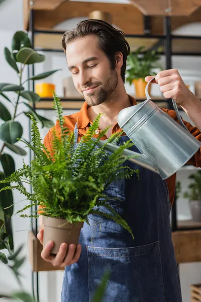 Junge brünette Floristin gießt Pflanze in Blumenladen — Stockfoto